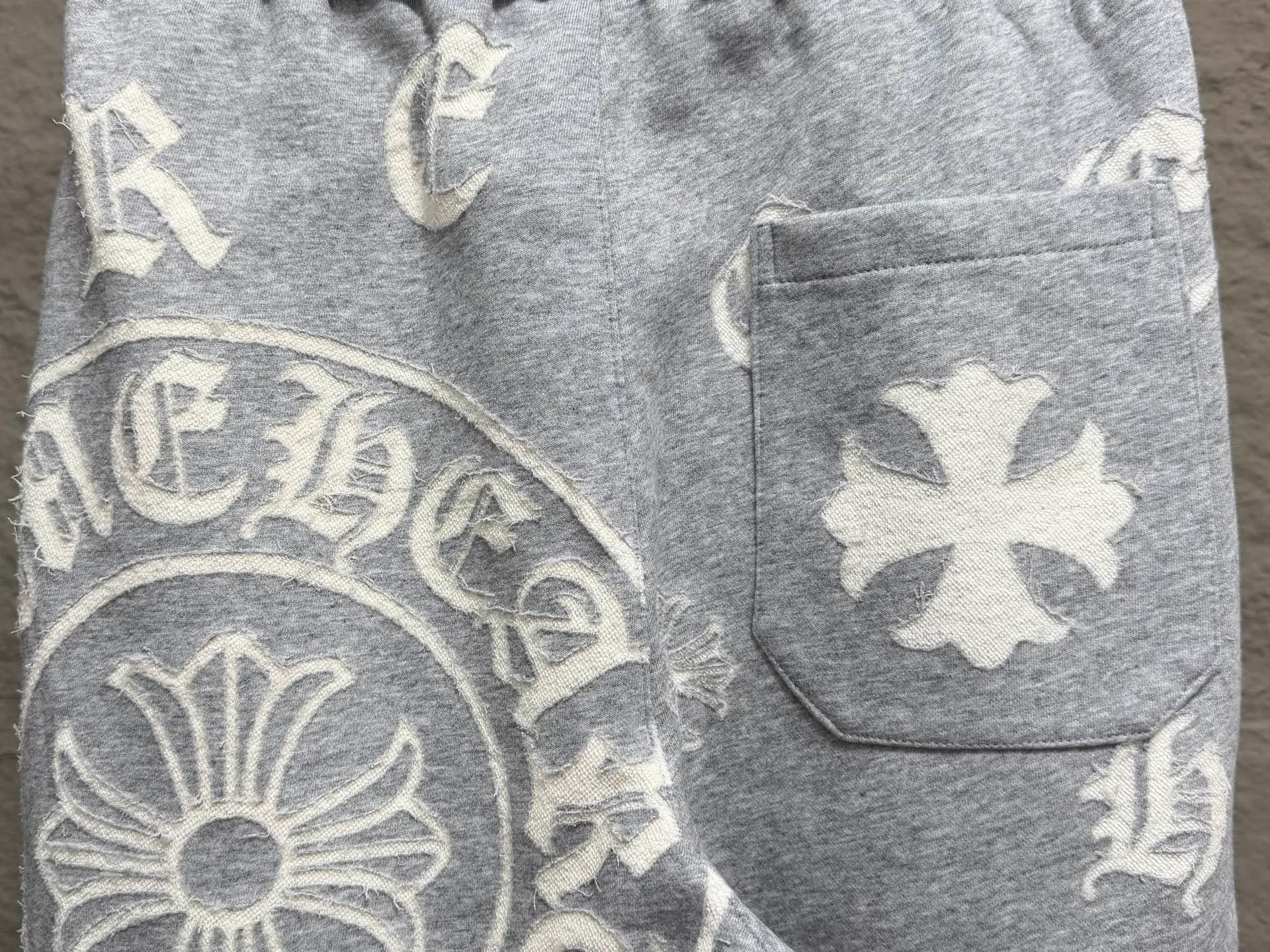 CH/Cro Heart 2026ss Burnt Flower Straight-leg Sweatpants Classic heavy-weight sweatpants with gray tones, Retro street style full-fitting, direct recognition, same style for men and women. ●Three-dimensional patchwork technology: The whole body is covered with Gothic letters + cross flower totems, using raw edge patchwork embroidery, with a mustache-like old texture, and uneven and layered patterns. It is not an ordinary print, and it is durable and not easy to fall off. ●Style tailoring: Loose, straight and wide-legged version, modifying the shape of the legs, hiding the flesh neatly, not flattering the figure, with an online drape, and the upper body has a relaxed street tone. ●Fabric and waist: Heavy knitted terry fabric, thick and soft, with good drape; elastic drawstring waist, with branded metal engraved rope ends, easy to put on and take off, and strong waist adaptability. ●Detailed design: The side pockets are convenient for carrying items, and the back pocket is decorated with cross-pattern patches. The front and rear patterns echo each other. Every detail is highly recognizable to the brand. ●Wearing scenarios: Suitable for street wear, daily outings, and trendy wear. Paired with sweaters, denim jackets, and leather jackets, you can easily create an American retro cool style. ●The overall gray base is paired with Cream White patches, which are low-key yet impactful. They are both comfortable and trendy. Versatile sweatpants, a must-have for fashionistas, are also available at the counter. SIZE：M L XL XXL XXXL